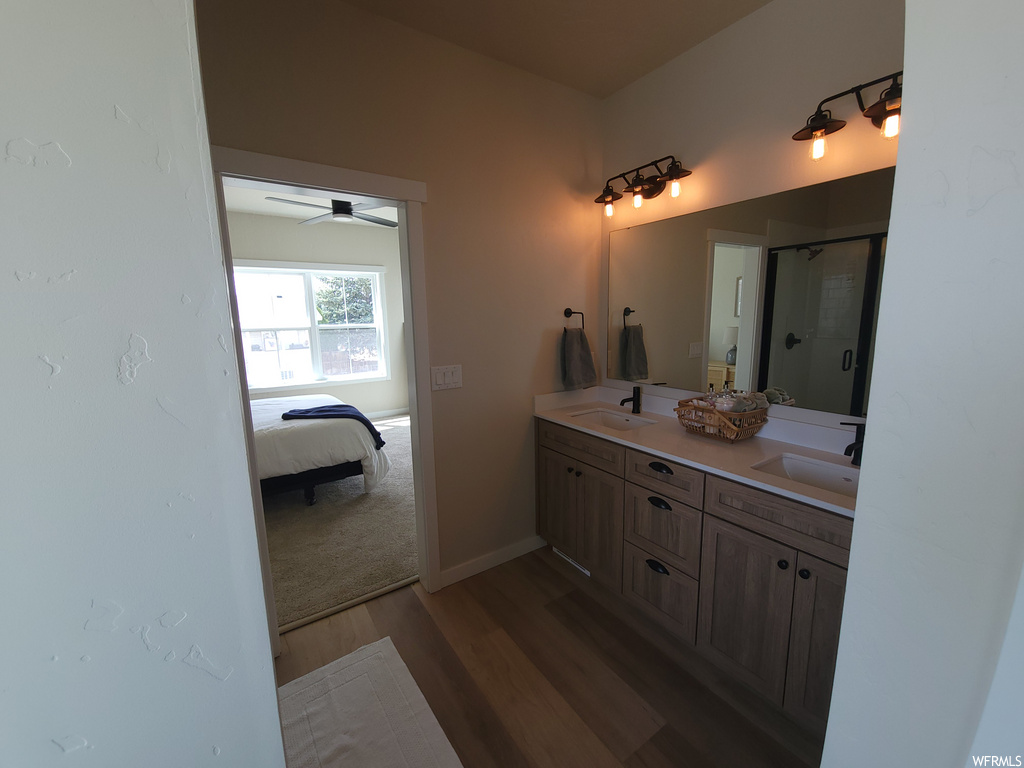 Bathroom featuring hardwood floors, a ceiling fan, dual large vanity, shower booth, and dual mirrors
