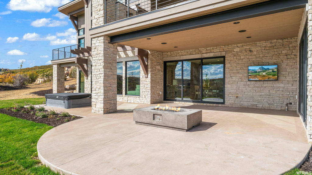 View of patio with a balcony, a hot tub, and an outdoor fire pit
