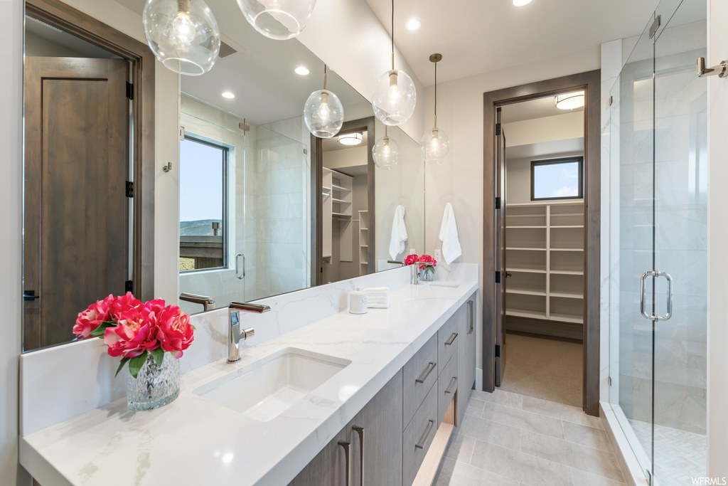 Bathroom featuring an enclosed shower, double sink vanity, mirror, and light tile flooring
