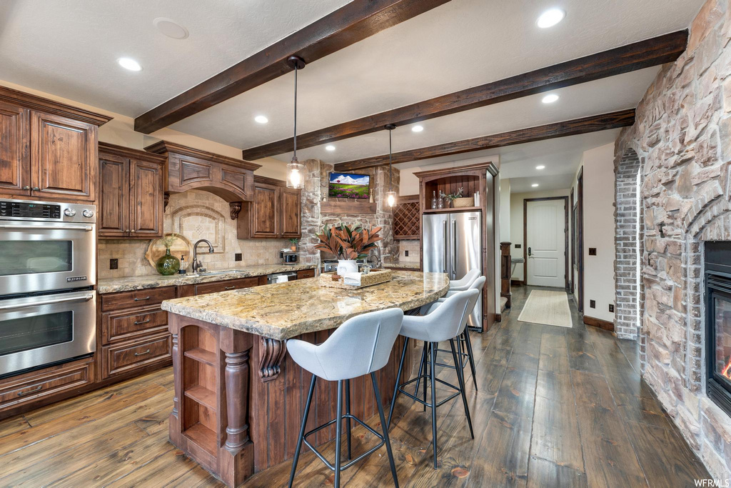 kitchen with wood-type flooring, a kitchen island, a breakfast bar area, stainless steel double oven, pendant lighting, and light granite-like countertops