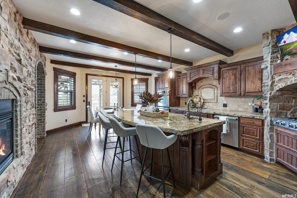 kitchen with natural light, a fireplace, a kitchen island, a breakfast bar area, oven, dishwasher, light stone countertops, and dark hardwood floors