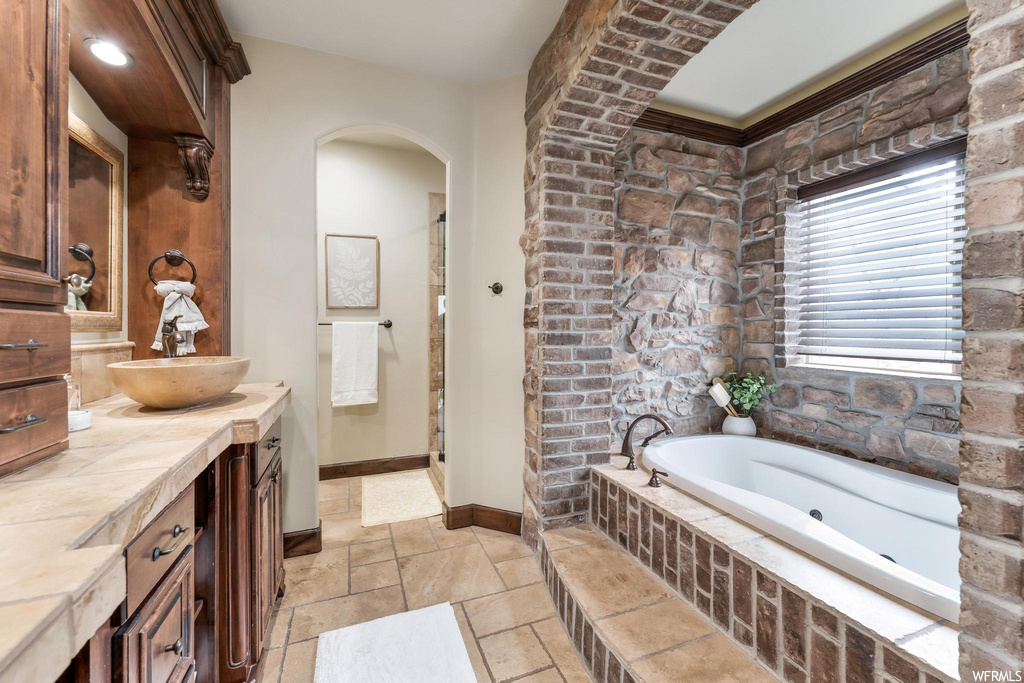 bathroom featuring exposed bricks, a tub, vanity with extensive cabinet space, and mirror