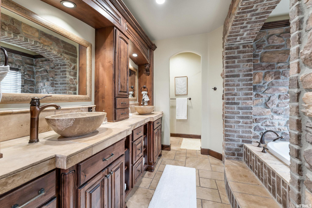 bathroom with tile floors, exposed bricks, mirror, a bath, and dual vanity