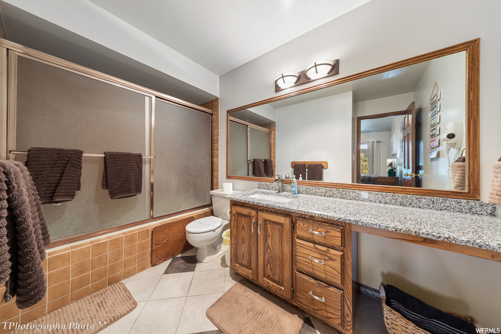 full bathroom with tile flooring, toilet, vanity, mirror, and enclosed tub / shower combo