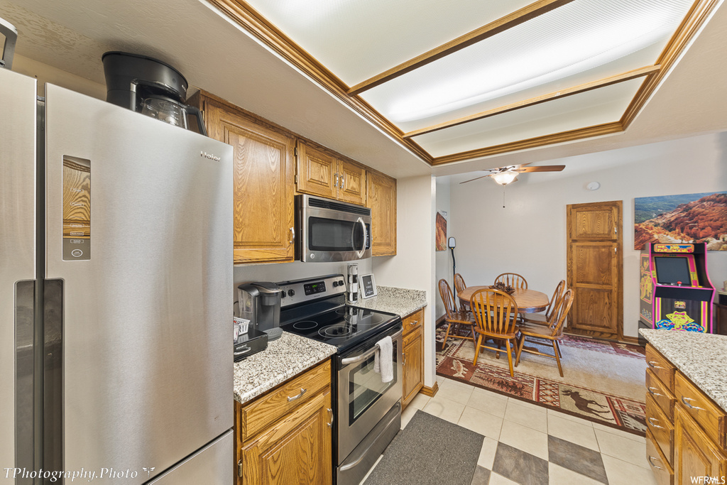 kitchen featuring a ceiling fan, refrigerator, electric range oven, microwave, brown cabinets, light tile flooring, and light countertops