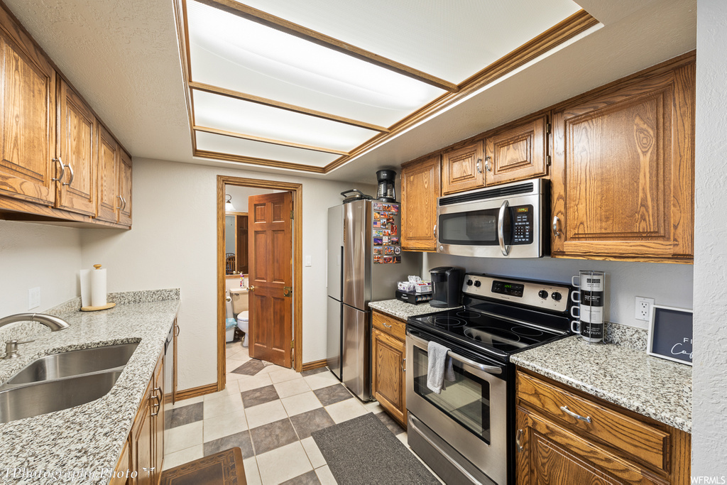 kitchen featuring refrigerator, electric range oven, microwave, brown cabinetry, light countertops, and light tile floors