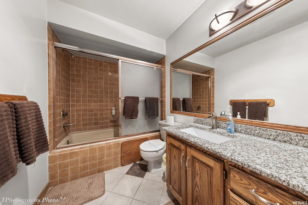 full bathroom with tile floors, toilet, vanity, mirror, and enclosed tub / shower combo