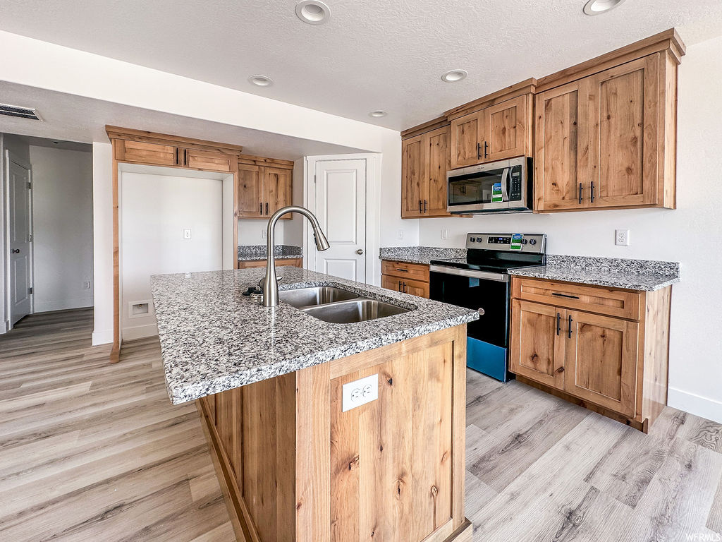 Kitchen with microwave, electric range oven, granite-like countertops, brown cabinets, and light hardwood flooring