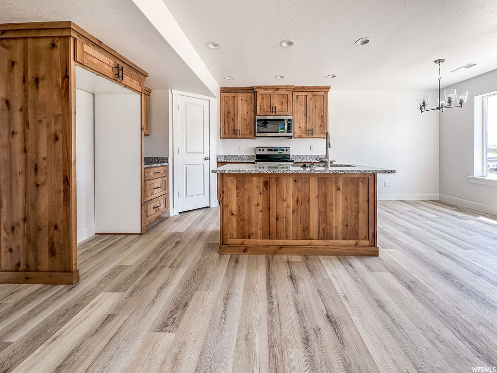 Kitchen with natural light, range oven, stainless steel microwave, light hardwood floors, brown cabinetry, and light countertops