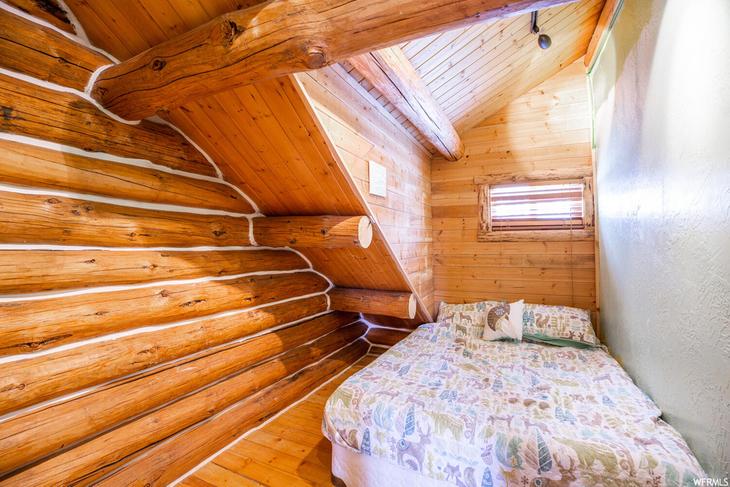 Unfurnished bedroom with wood ceiling, wood walls, vaulted ceiling with beams, and hardwood / wood-style flooring
