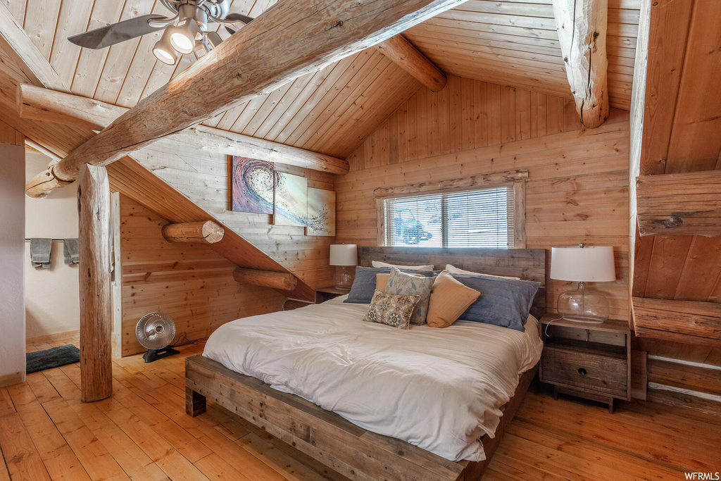 Bedroom with wooden walls, light wood-type flooring, wooden ceiling, vaulted ceiling with beams, and ceiling fan