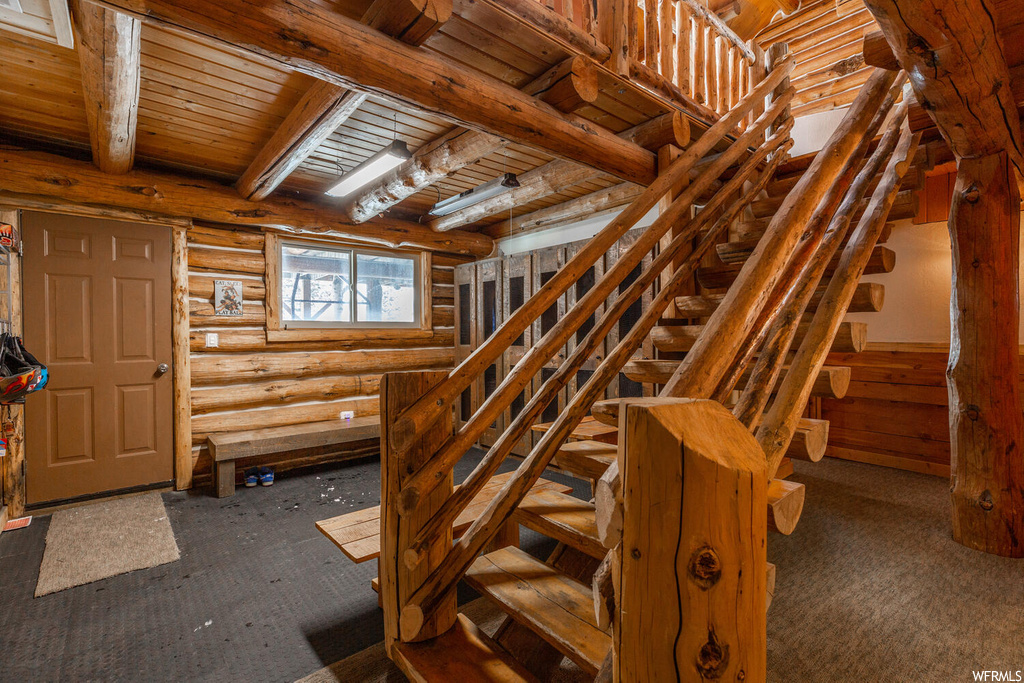 Stairs featuring beamed ceiling, log walls, dark carpet, and wooden ceiling
