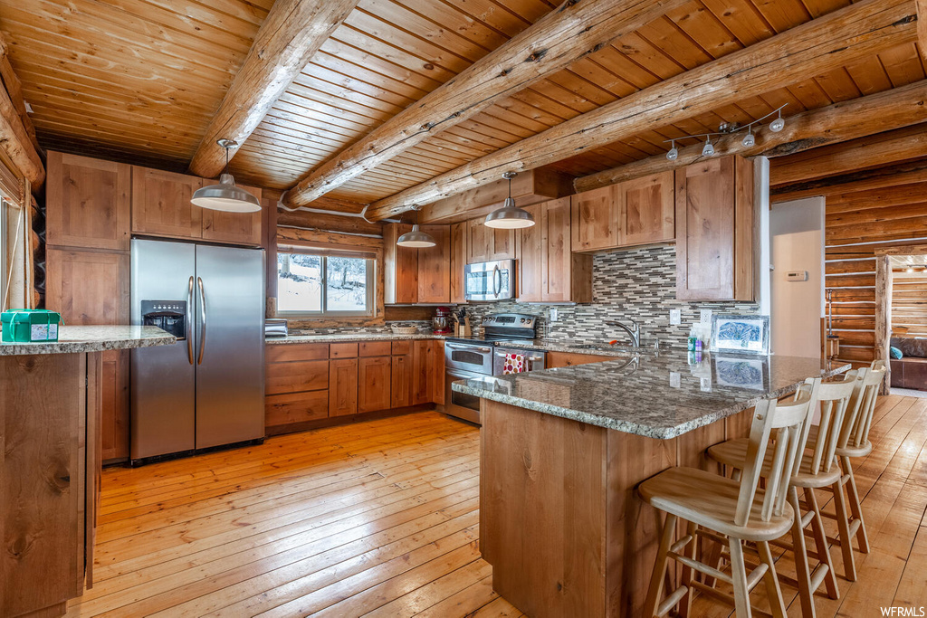 Kitchen featuring decorative light fixtures, light wood-type flooring, log walls, stainless steel appliances, and beam ceiling