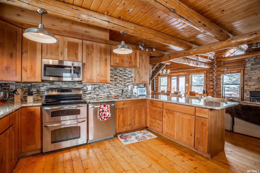 Kitchen with light hardwood / wood-style flooring, beam ceiling, stainless steel appliances, and rustic walls