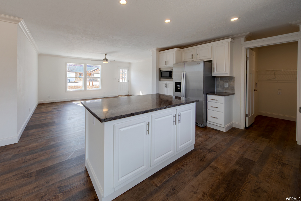 kitchen featuring a kitchen island, natural light, refrigerator, microwave, dark countertops, white cabinetry, and dark hardwood flooring