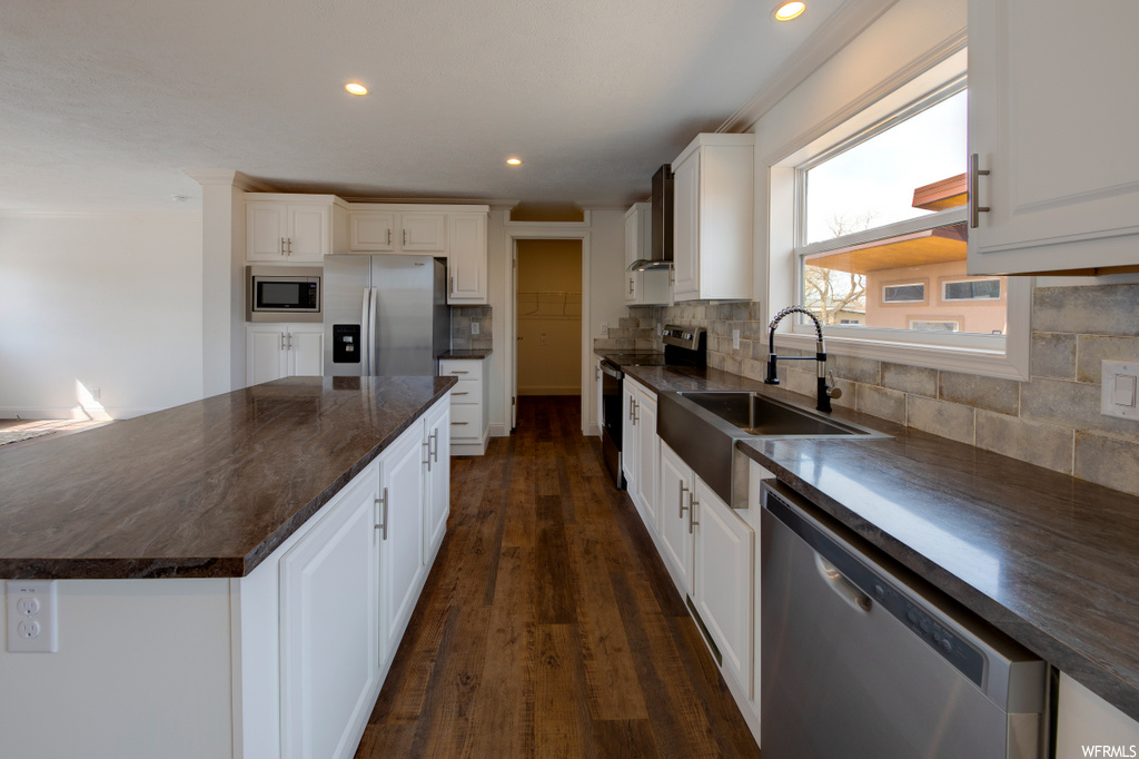 kitchen with natural light, refrigerator, range oven, dishwasher, microwave, dark countertops, white cabinetry, and dark hardwood flooring