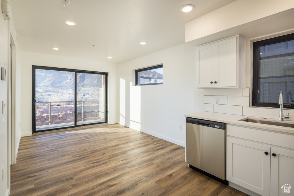 Kitchen with dishwasher, a sink, wood finished floors, white cabinets, and baseboards