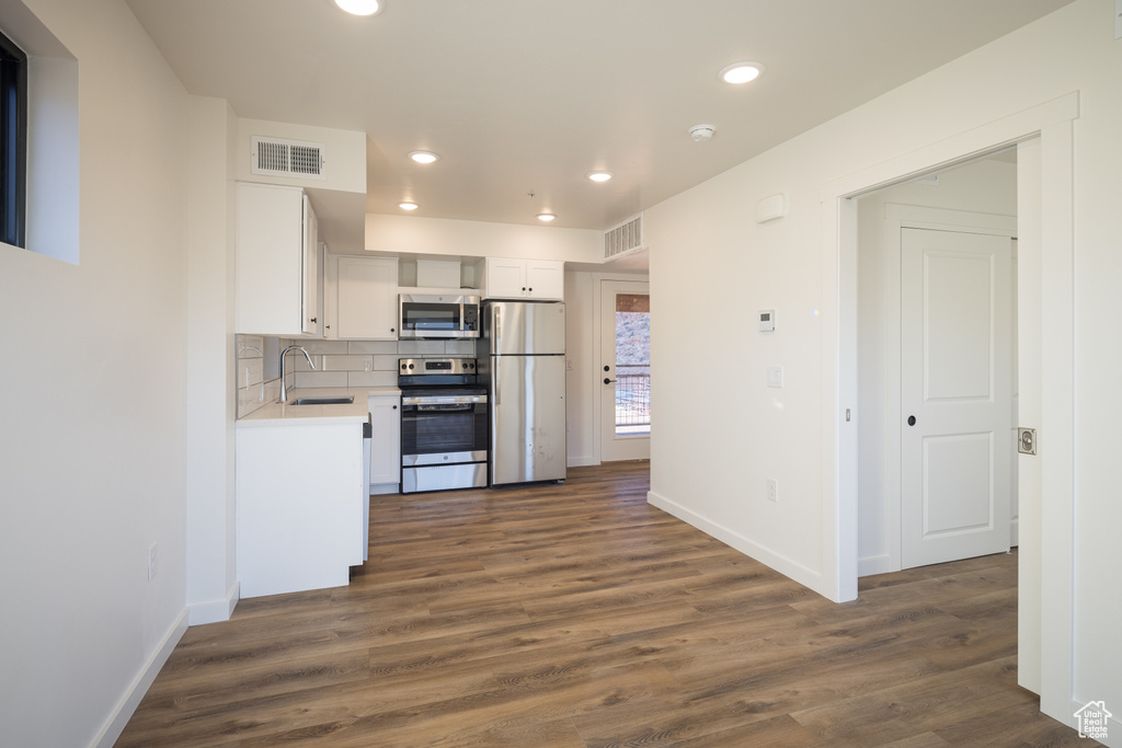 Kitchen featuring stainless steel appliances, a sink, light countertops, baseboards, and dark wood-style flooring