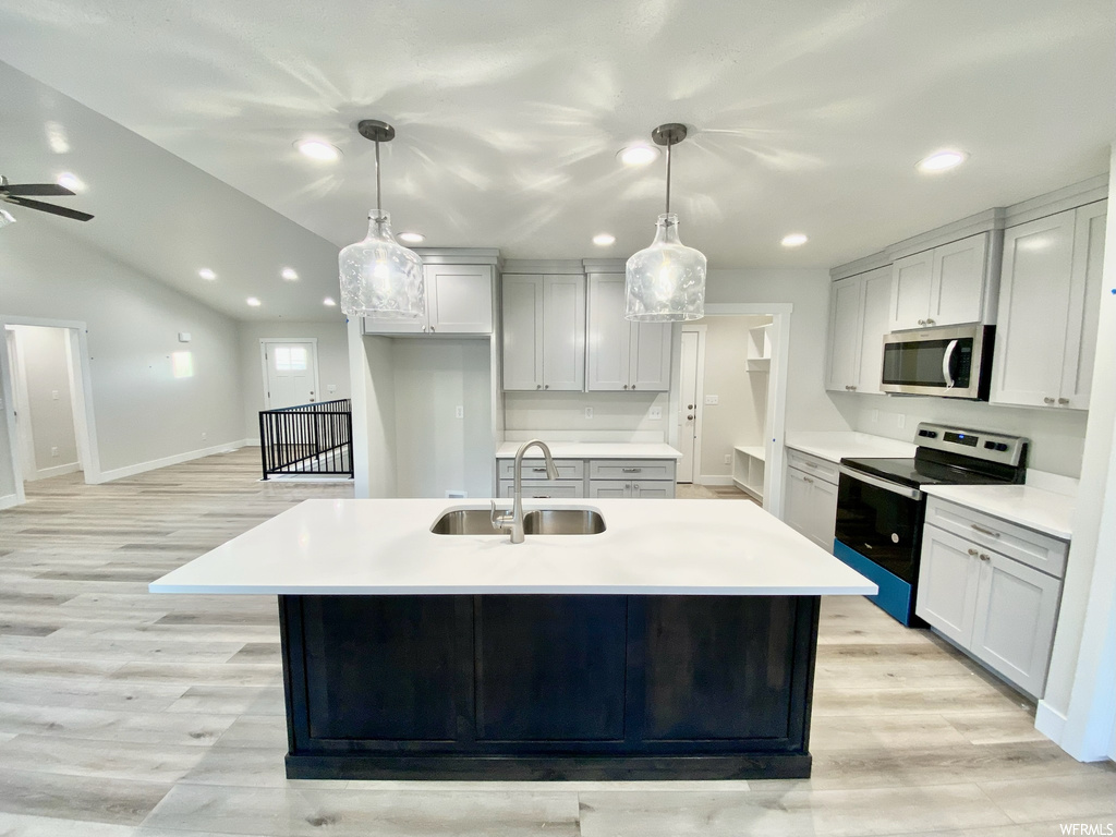 Kitchen with vaulted ceiling, light countertops, light hardwood floors, white cabinetry, appliances with stainless steel finishes, ceiling fan, and pendant lighting