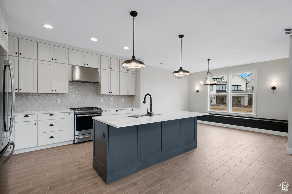 Kitchen featuring stainless steel gas stove, white cabinets, decorative light fixtures, and sink