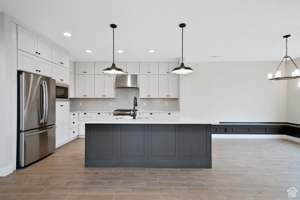 Kitchen with white cabinets, sink, a center island with sink, hanging light fixtures, and stainless steel refrigerator