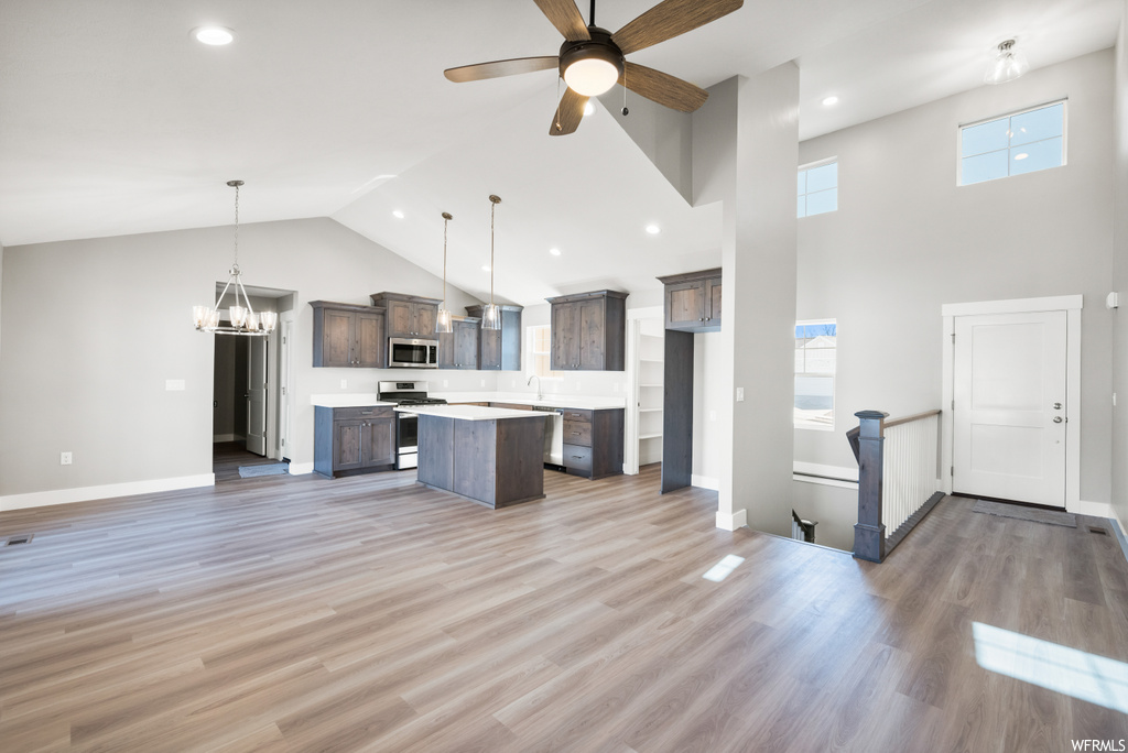 kitchen with lofted ceiling, a ceiling fan, microwave, dishwasher, range oven, dark brown cabinets, pendant lighting, light countertops, and light hardwood flooring