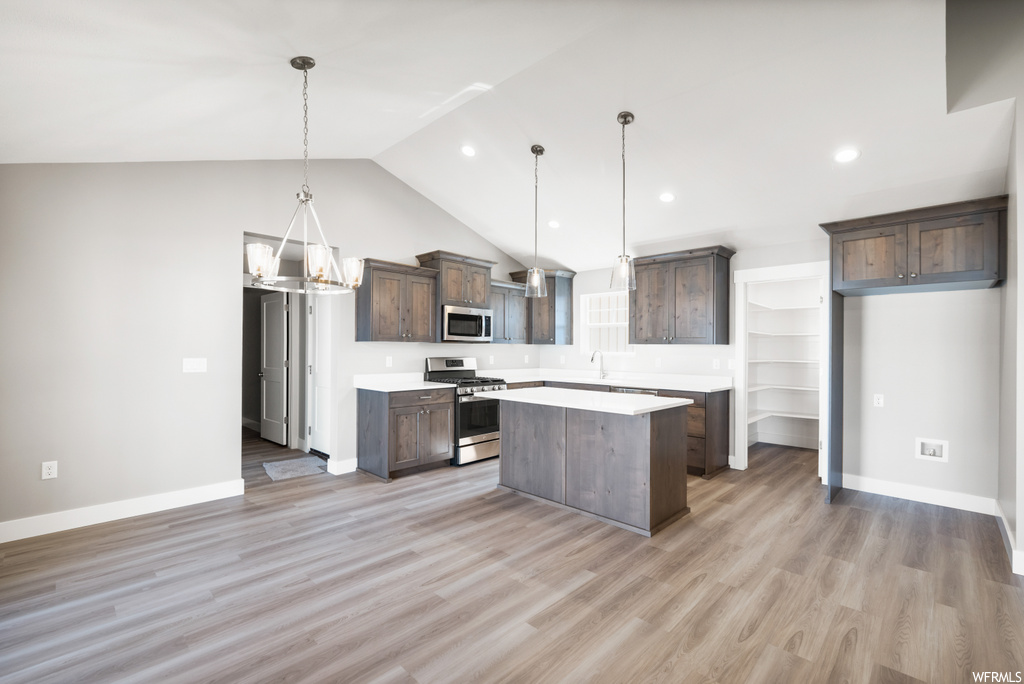 kitchen featuring lofted ceiling, stainless steel microwave, range oven, dark brown cabinets, pendant lighting, light countertops, and light hardwood floors
