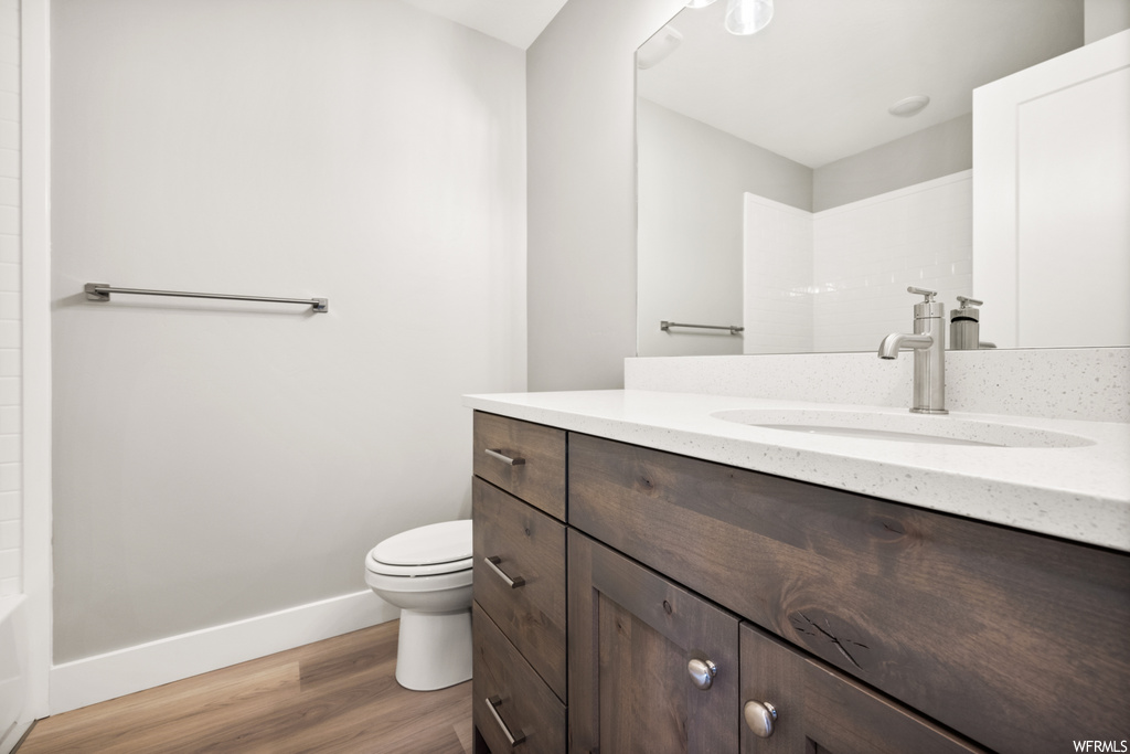 half bath featuring hardwood floors, mirror, vanity, and toilet