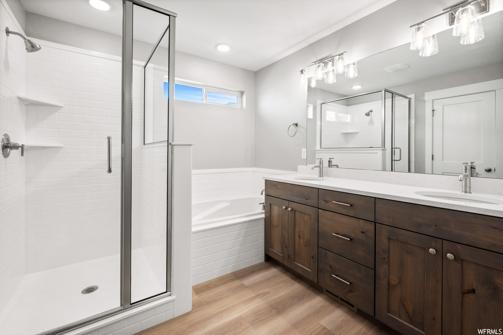 bathroom featuring hardwood flooring, dual mirrors, double large vanities, double sink, and independent shower and bath