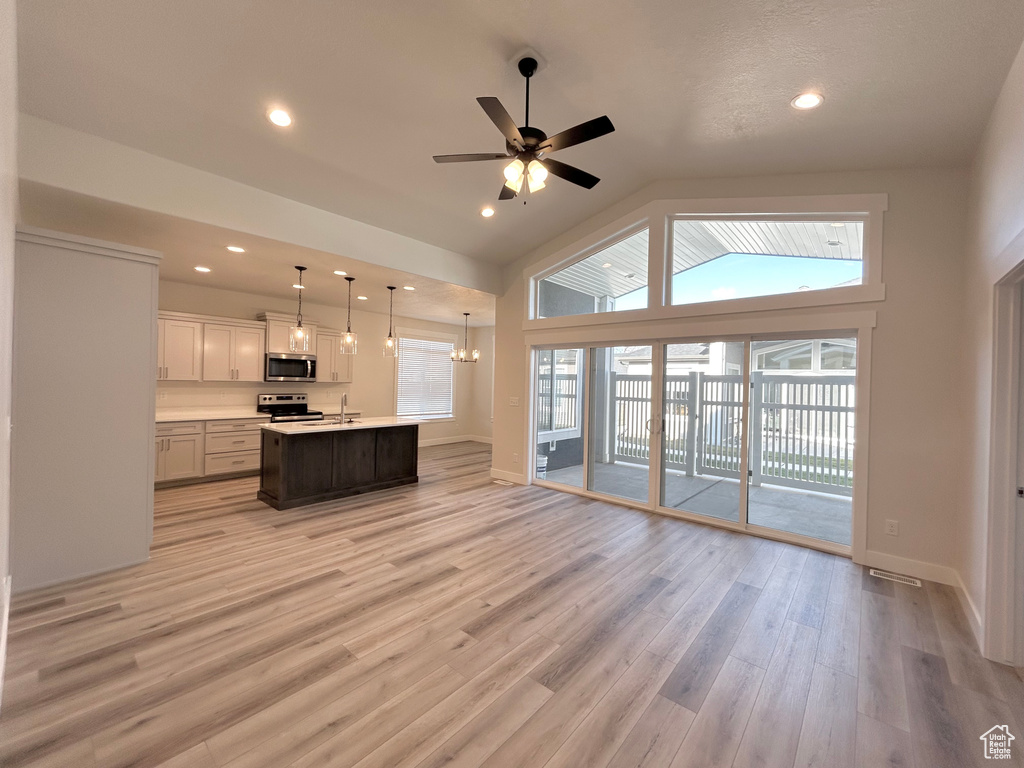 Kitchen featuring hanging light fixtures, appliances with stainless steel finishes, light hardwood / wood-style flooring, ceiling fan, and a center island with sink