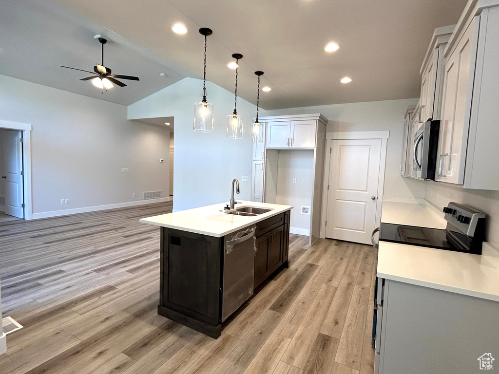 Kitchen featuring ceiling fan, light wood-type flooring, appliances with stainless steel finishes, hanging light fixtures, and an island with sink