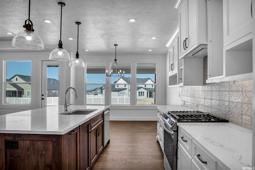 Kitchen featuring dark hardwood / wood-style flooring, appliances with stainless steel finishes, pendant lighting, an island with sink, and backsplash