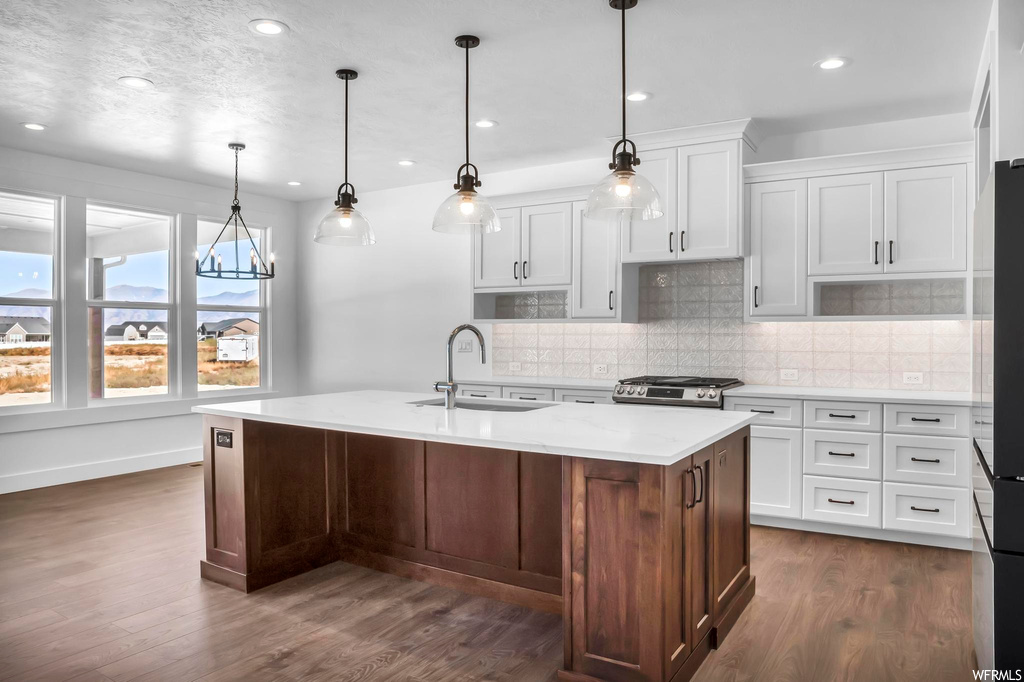 Kitchen featuring sink, a kitchen island with sink, pendant lighting, stove, and dark hardwood / wood-style floors
