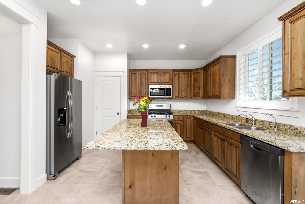 kitchen featuring natural light, refrigerator, range oven, stainless steel dishwasher, microwave, brown cabinets, stone countertops, and light tile floors