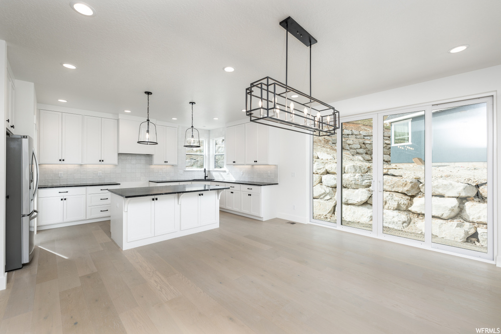 kitchen featuring natural light, a kitchen island, refrigerator, light countertops, pendant lighting, white cabinets, and light parquet floors