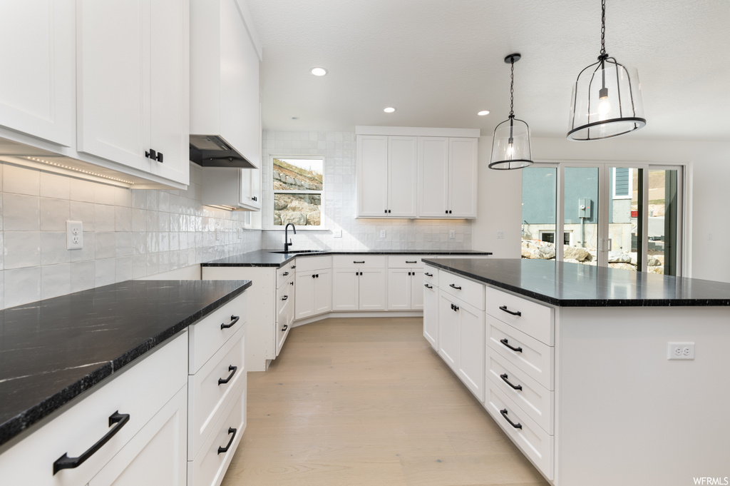 kitchen with a wealth of natural light, wood-type flooring, range hood, dark countertops, and white cabinetry
