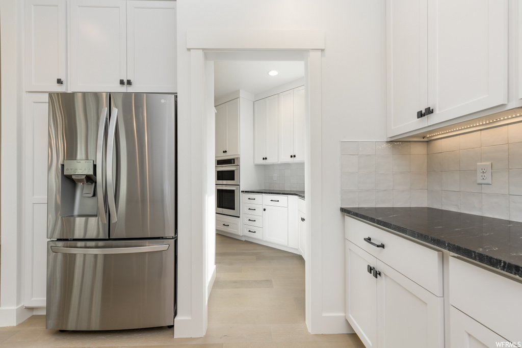 kitchen featuring double oven, refrigerator, white cabinetry, dark countertops, and light tile floors