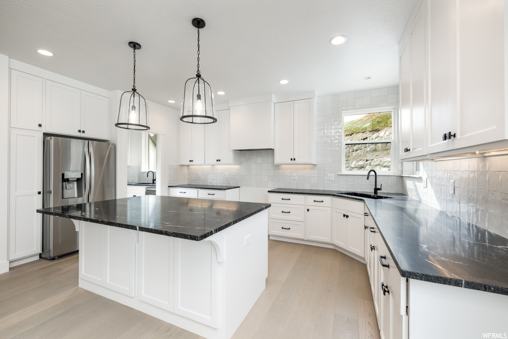 kitchen featuring stainless steel finishes, white cabinets, an island with sink, dark stone countertops, and light hardwood floors