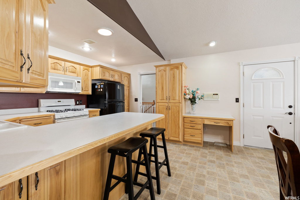 kitchen featuring a kitchen bar, refrigerator, microwave, gas range oven, light countertops, and light floors