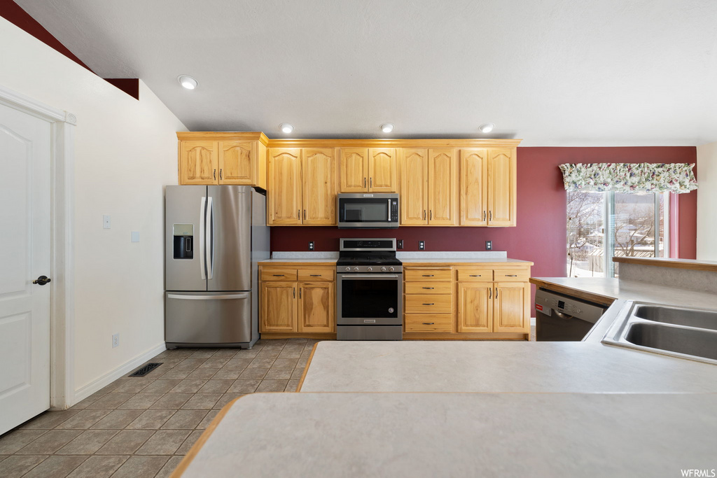 kitchen with natural light, stainless steel refrigerator, range oven, microwave, dishwasher, light countertops, light tile floors, and brown cabinets