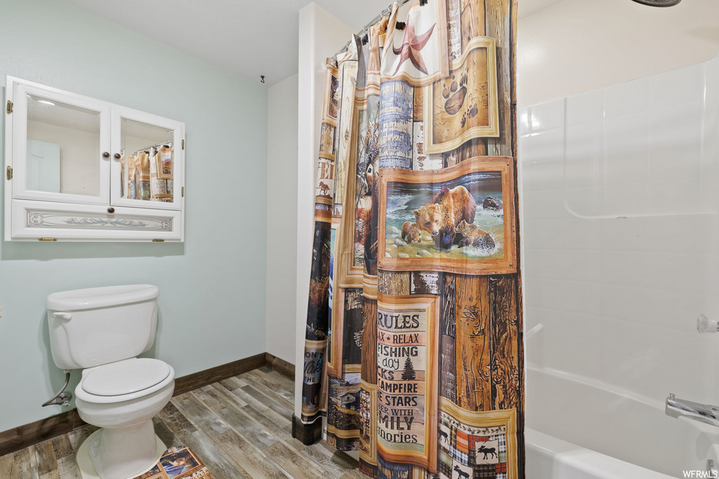 bathroom featuring wood-type flooring, shower / bathing tub combination, shower curtain, and toilet