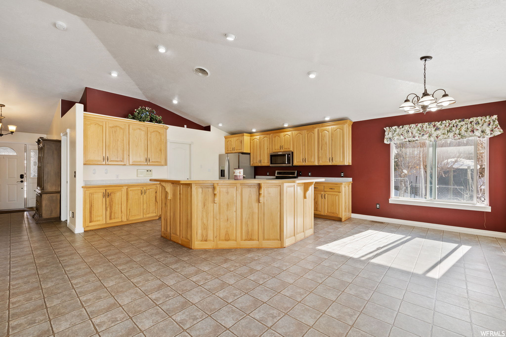 kitchen with natural light, lofted ceiling, refrigerator, microwave, brown cabinetry, and light tile floors