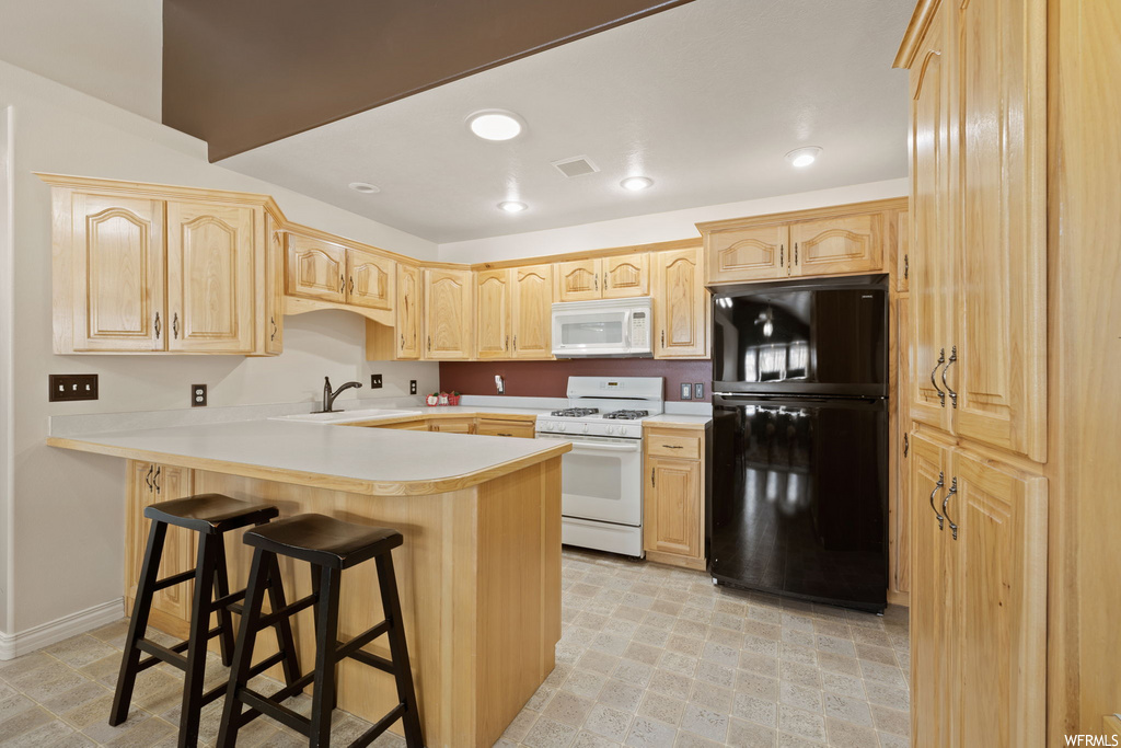 kitchen with a kitchen bar, refrigerator, microwave, gas range oven, light countertops, and light tile floors