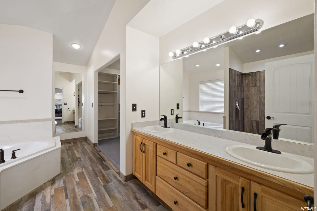 bathroom featuring hardwood floors, dual mirrors, his and hers vanity, and a bath