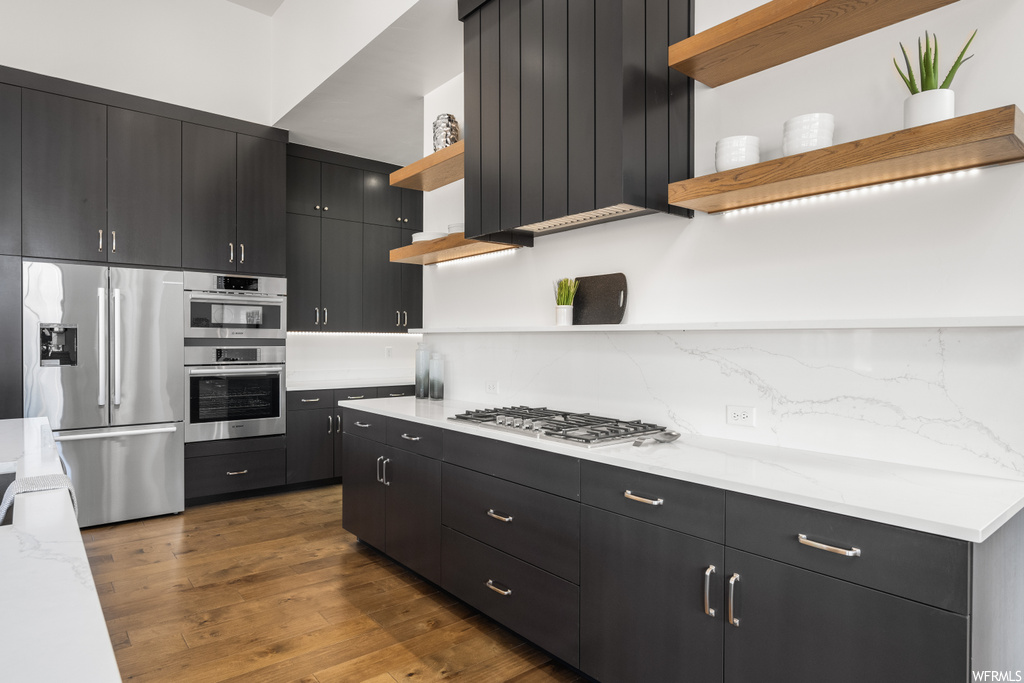 Kitchen featuring light parquet floors, stainless steel appliances, backsplash, dark brown cabinetry, and light countertops