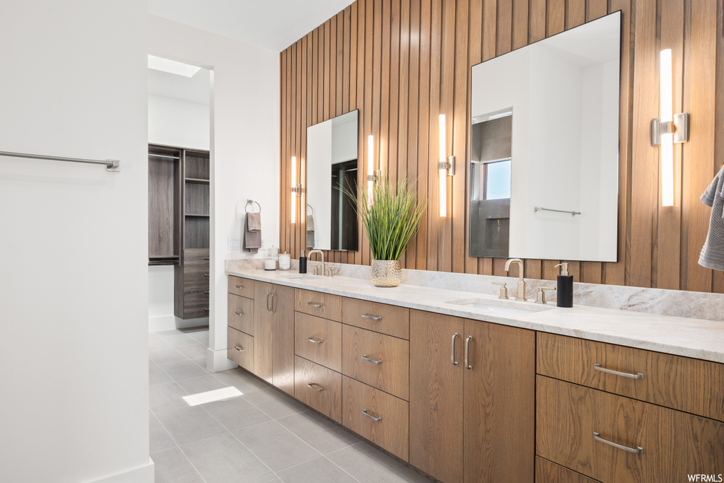 Bathroom featuring light tile floors, dual bowl vanity, and mirror