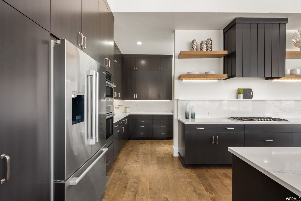 Kitchen featuring high end fridge, dark brown cabinets, gas stovetop, light countertops, and light hardwood flooring