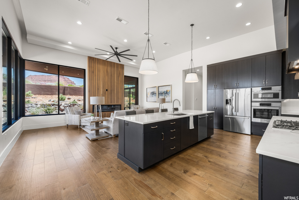Kitchen featuring light parquet floors, dark brown cabinetry, light countertops, decorative light fixtures, and appliances with stainless steel finishes