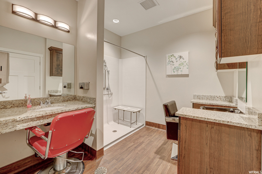 bathroom featuring hardwood floors, a shower, vanity, and dual mirrors