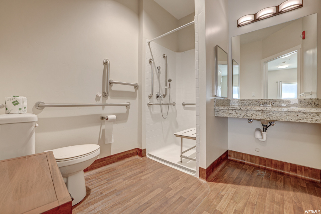 bathroom with hardwood flooring, toilet, vanity, mirror, and a shower